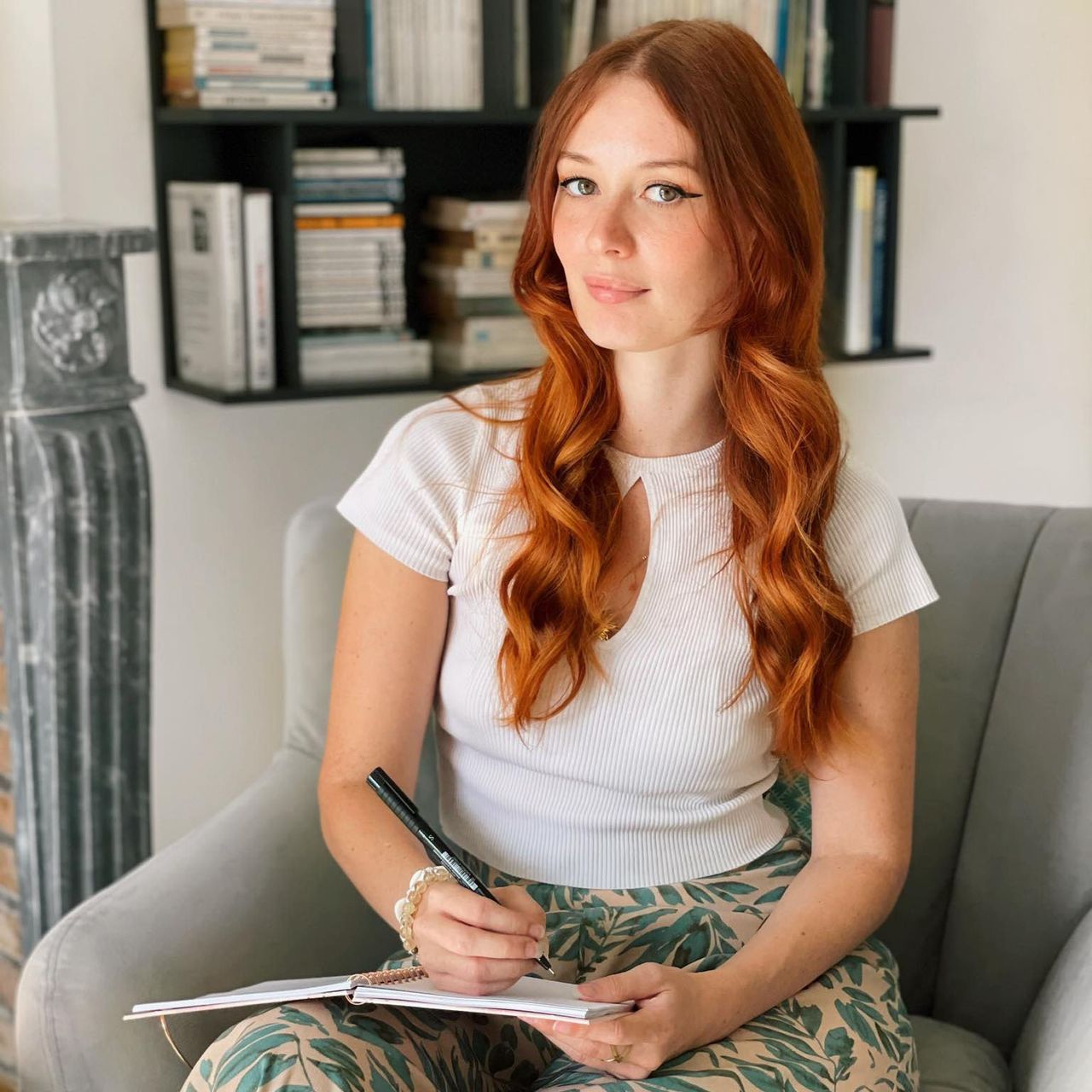 Femme rousse assise qui écrit sur un carnet en regardant l'objectif